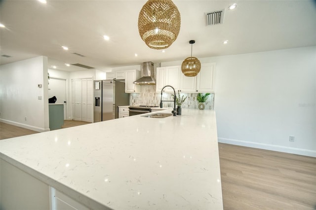 kitchen featuring wall chimney range hood, a sink, baseboards, stainless steel refrigerator with ice dispenser, and visible vents