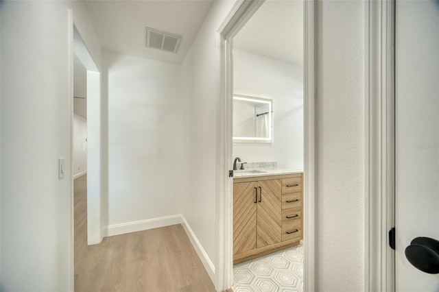 hallway with baseboards, visible vents, a sink, and light wood-style floors