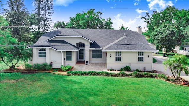 ranch-style home featuring stucco siding, roof with shingles, a patio area, a front lawn, and a chimney