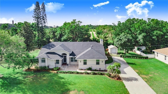 view of front of property featuring a chimney, an outdoor structure, fence, a front lawn, and driveway
