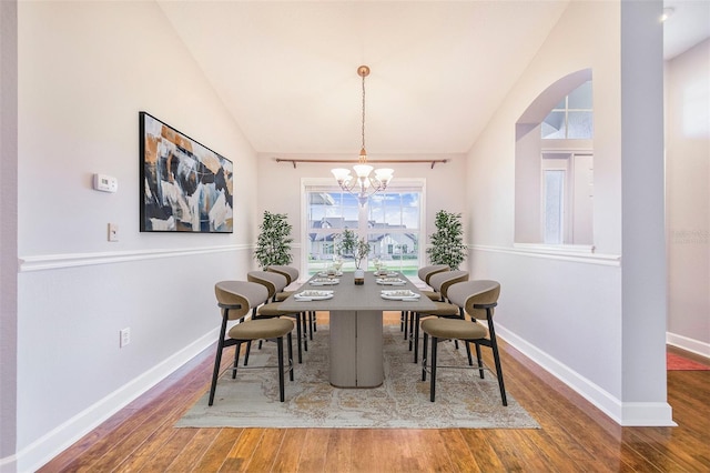 dining area featuring a chandelier, arched walkways, wood finished floors, and baseboards