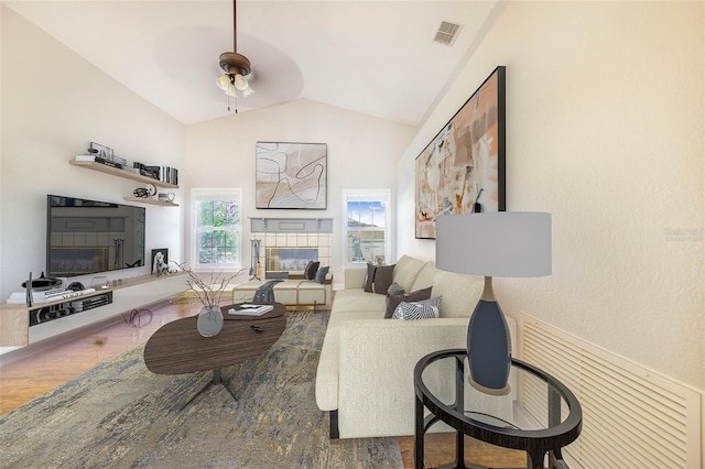 living area with a fireplace, a ceiling fan, visible vents, lofted ceiling, and wood finished floors
