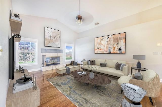 living area featuring a ceiling fan, vaulted ceiling, visible vents, wood finished floors, and a tile fireplace