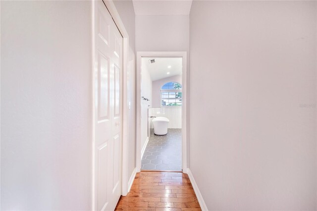 corridor featuring light wood-type flooring, baseboards, and vaulted ceiling