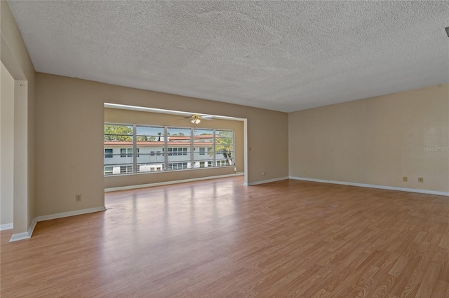 spare room featuring light wood-style flooring, baseboards, and a textured ceiling