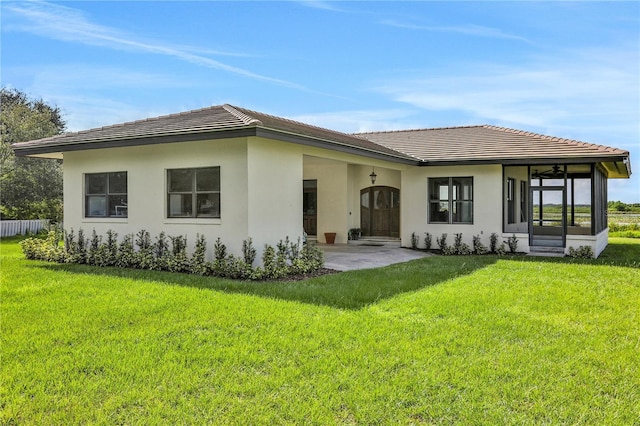 rear view of property featuring a sunroom, a yard, stucco siding, and a tiled roof