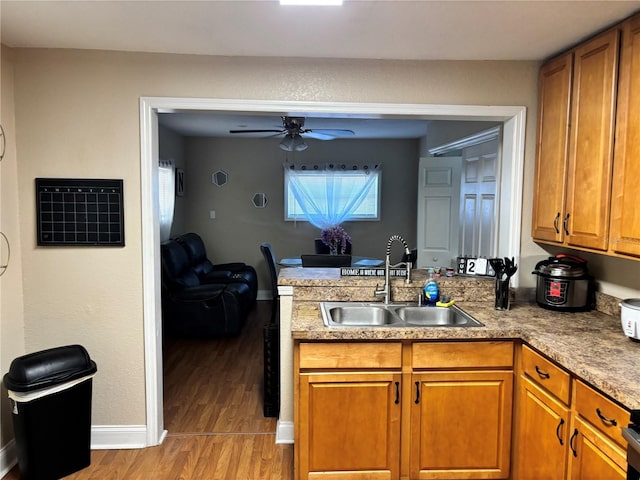 kitchen featuring light wood finished floors, a ceiling fan, a sink, a peninsula, and brown cabinetry