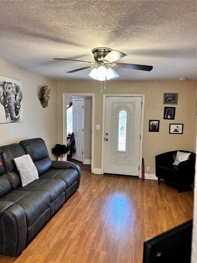 living area featuring ceiling fan, baseboards, wood finished floors, and a textured ceiling