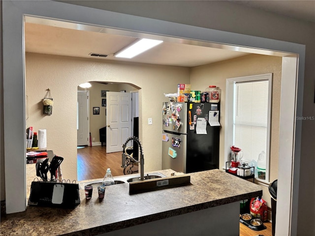 kitchen featuring wood finished floors, visible vents, a sink, arched walkways, and freestanding refrigerator