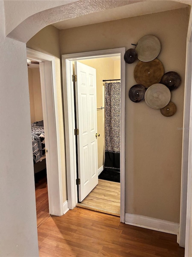 hall with arched walkways, light wood finished floors, and baseboards