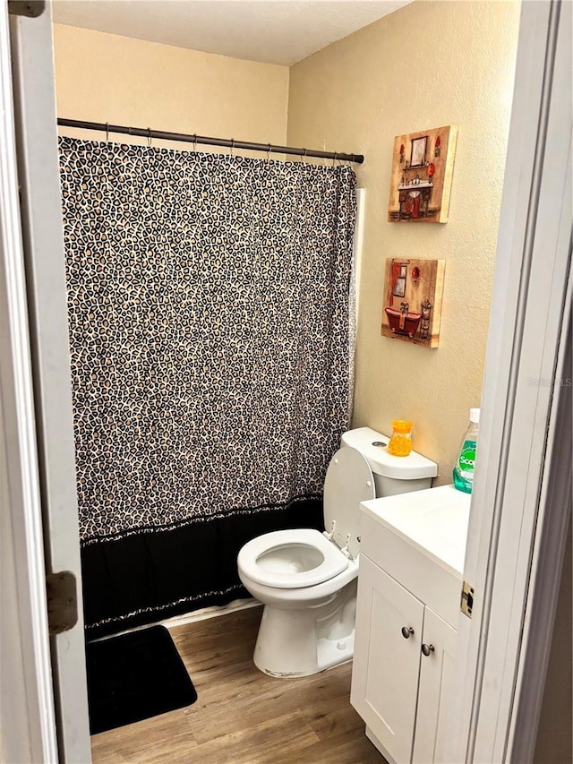 full bath with wood finished floors, vanity, a shower with curtain, a textured wall, and toilet
