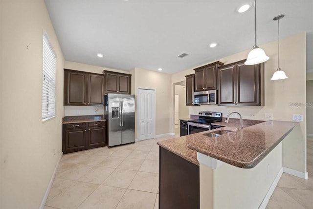 kitchen with dark brown cabinets, appliances with stainless steel finishes, dark stone countertops, and a sink