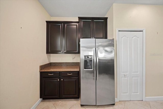kitchen with stainless steel refrigerator with ice dispenser, baseboards, dark countertops, and light tile patterned flooring