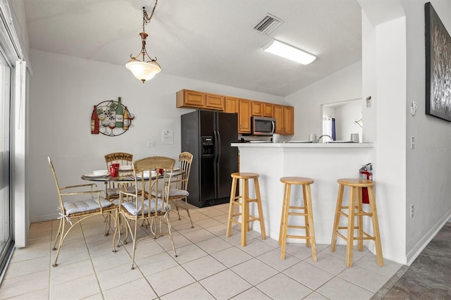 kitchen featuring stainless steel microwave, black fridge with ice dispenser, visible vents, a breakfast bar area, and lofted ceiling