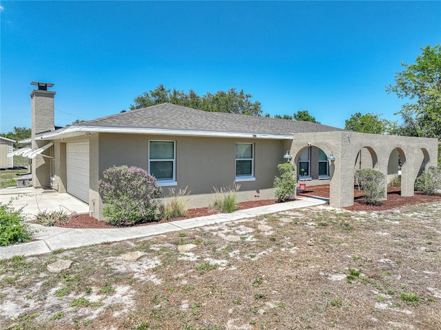 back of house with a chimney, a shingled roof, stucco siding, an attached garage, and driveway