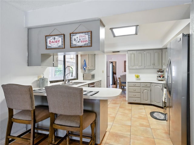 kitchen with a peninsula, freestanding refrigerator, a sink, and gray cabinetry
