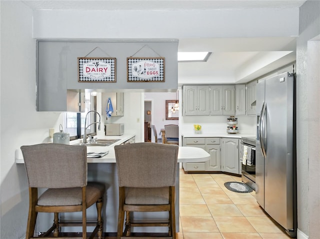 kitchen with stainless steel appliances, a breakfast bar, light countertops, a sink, and a peninsula