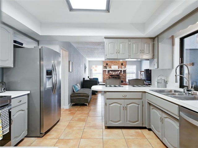 kitchen featuring stainless steel appliances, light countertops, a sink, gray cabinetry, and a peninsula