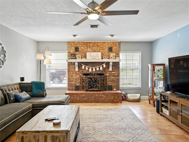 living area with a fireplace, a textured ceiling, tile patterned flooring, and ceiling fan