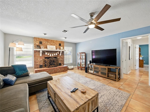 living area featuring a textured ceiling, light tile patterned floors, ceiling fan, a fireplace, and visible vents