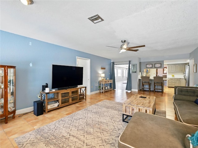 living area with visible vents, a ceiling fan, light tile patterned flooring, baseboards, and a textured ceiling