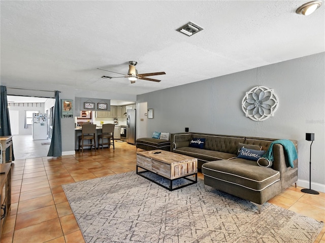 living room with ceiling fan, light tile patterned flooring, a textured ceiling, and visible vents