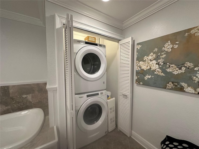 laundry room with dark tile patterned floors, stacked washing maching and dryer, and crown molding