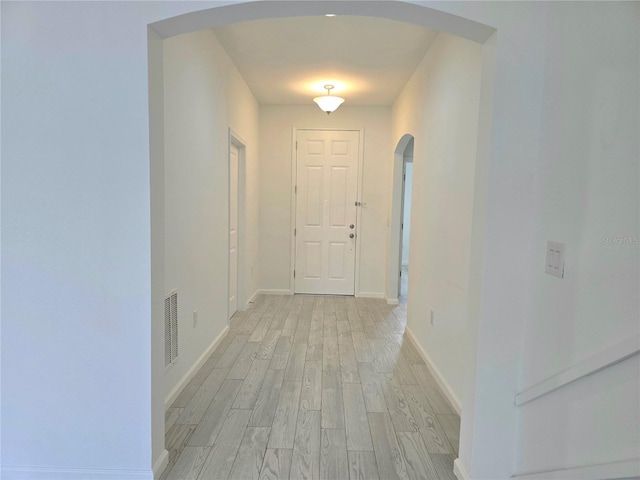 corridor with visible vents, baseboards, light wood-style flooring, and arched walkways