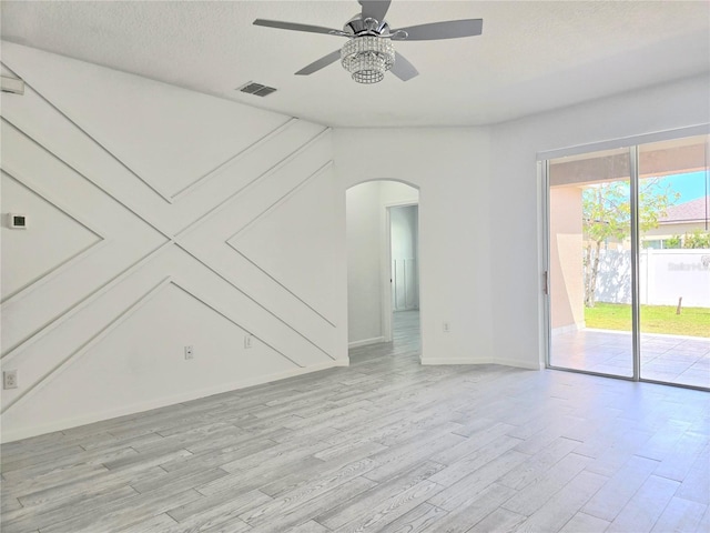 unfurnished living room with arched walkways, light wood-style flooring, baseboards, visible vents, and a ceiling fan