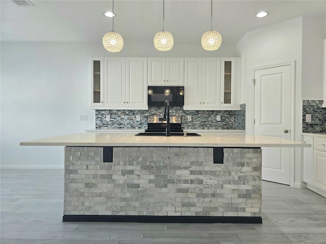 kitchen featuring decorative backsplash, glass insert cabinets, light wood-type flooring, black microwave, and white cabinetry