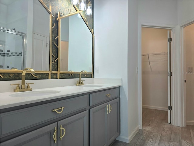 full bath featuring wood finished floors, a walk in closet, a stall shower, and a sink