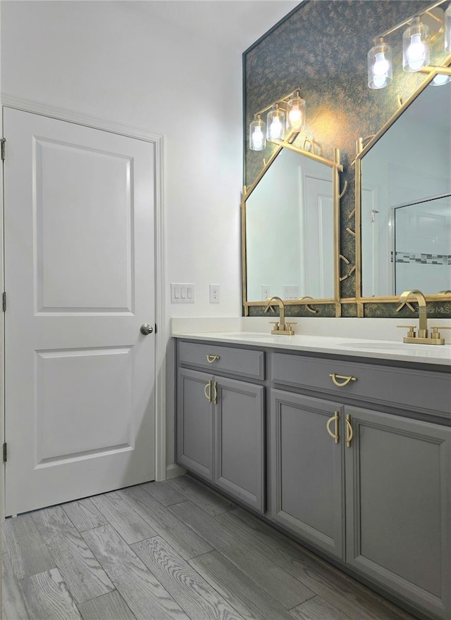 bathroom with wood finished floors, a shower with door, double vanity, and a sink