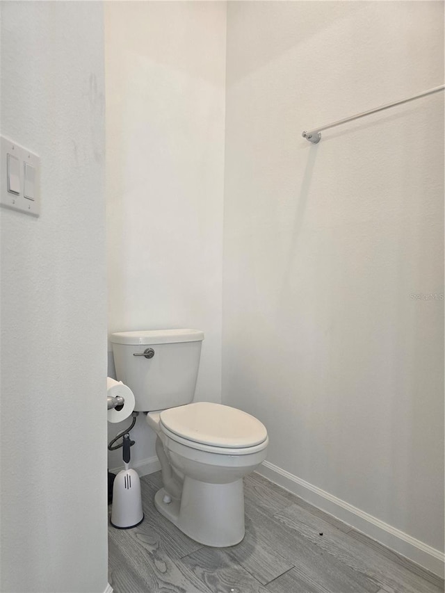 bathroom with baseboards, wood finished floors, and toilet