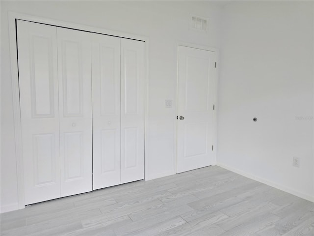 unfurnished bedroom featuring light wood finished floors, a closet, visible vents, and baseboards