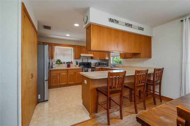 2390 Lake Easy Rd, Babson Park, FL 33827 - kitchen with visible vents, a peninsula, under cabinet range hood, brown cabinets, and appliances with stainless steel finishes