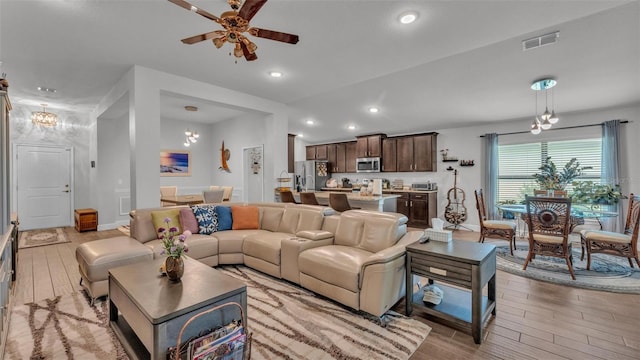 living area featuring visible vents, light wood-type flooring, recessed lighting, and ceiling fan with notable chandelier
