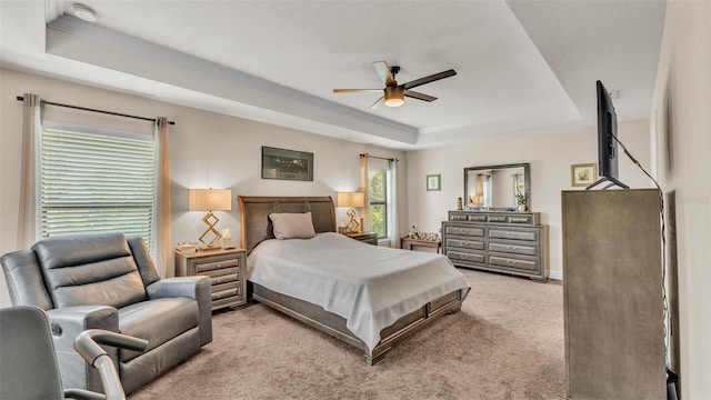 bedroom with a ceiling fan, light carpet, and a tray ceiling