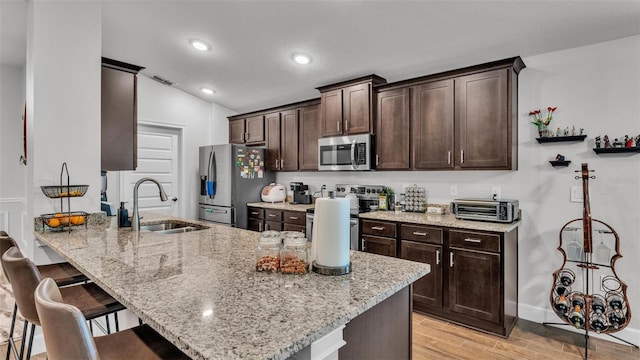 kitchen with a kitchen breakfast bar, a sink, visible vents, stainless steel appliances, and dark brown cabinetry