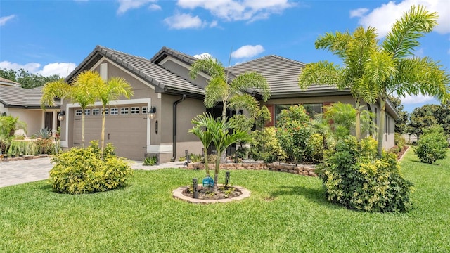 view of front facade with stucco siding, a tiled roof, driveway, a front lawn, and an attached garage