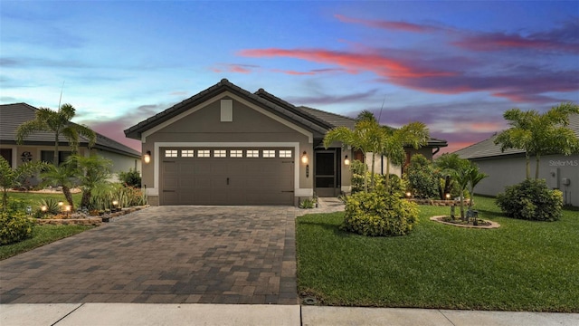 ranch-style home with stucco siding, decorative driveway, a yard, and an attached garage