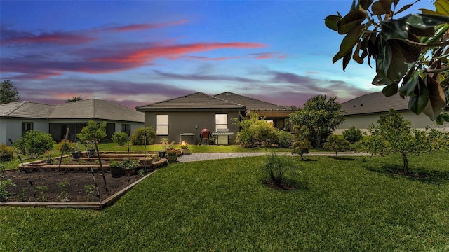 view of front of house with a tile roof, a garden, a lawn, central AC, and stucco siding