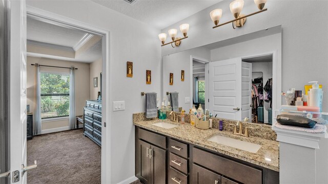 full bathroom with double vanity, a walk in closet, crown molding, and a sink