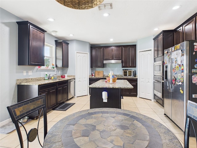 kitchen with light tile patterned floors, appliances with stainless steel finishes, visible vents, a kitchen island, and under cabinet range hood