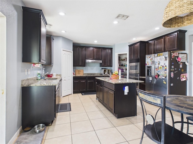 kitchen with light stone countertops, stainless steel appliances, a center island, dark brown cabinetry, and visible vents