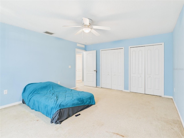 carpeted bedroom with visible vents, multiple closets, a ceiling fan, and baseboards