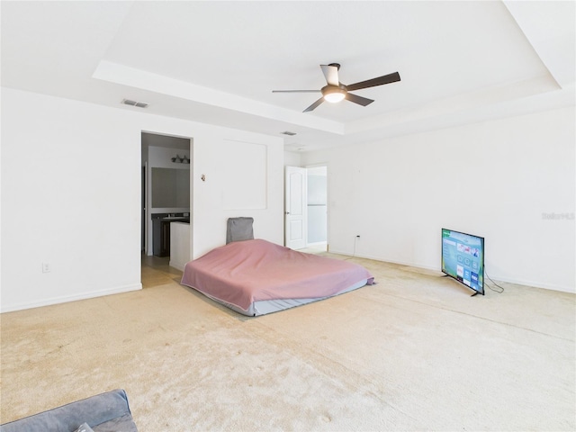 carpeted bedroom featuring connected bathroom, ceiling fan, a tray ceiling, visible vents, and baseboards