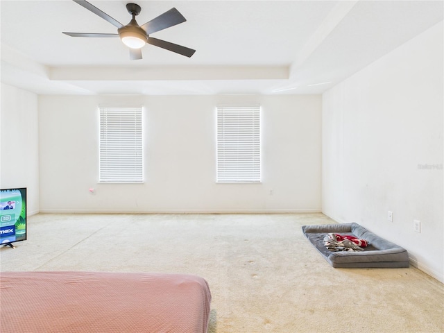 carpeted bedroom with a ceiling fan, a raised ceiling, and baseboards