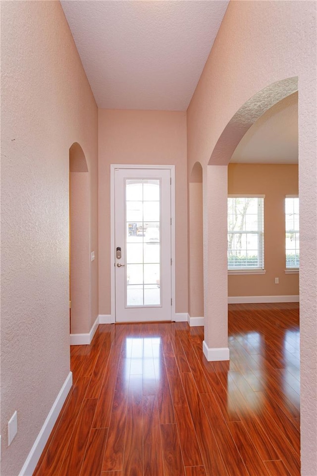 entryway with a textured wall, arched walkways, and dark wood-style flooring