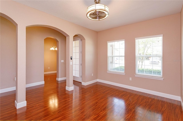 unfurnished room featuring arched walkways, wood finished floors, and baseboards