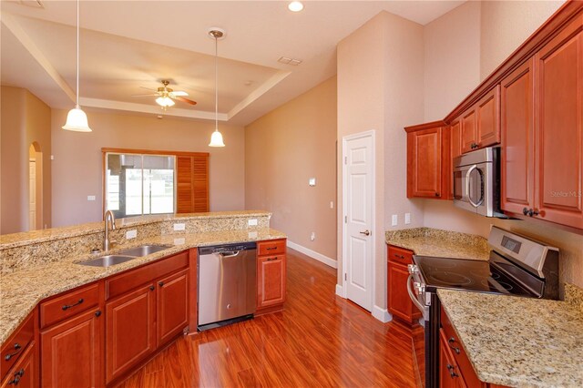 kitchen featuring stainless steel appliances, a tray ceiling, a ceiling fan, a sink, and dark wood-style flooring